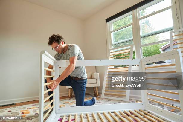 low angle shot of a man putting together a crib in a nursery for his new family member. - culla foto e immagini stock