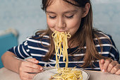 a child girl with a satisfied expression on her face eats dinner in the kitchen at home. Cute funny little girl eating spaghetti