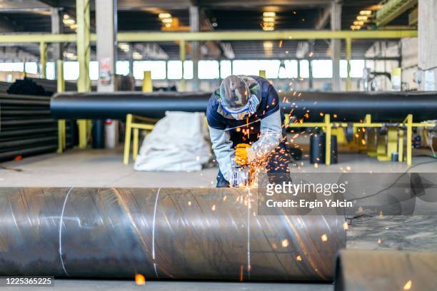 metal worker in protective suit and gloves cutting pipe with electric grinder - oil and gas workers imagens e fotografias de stock