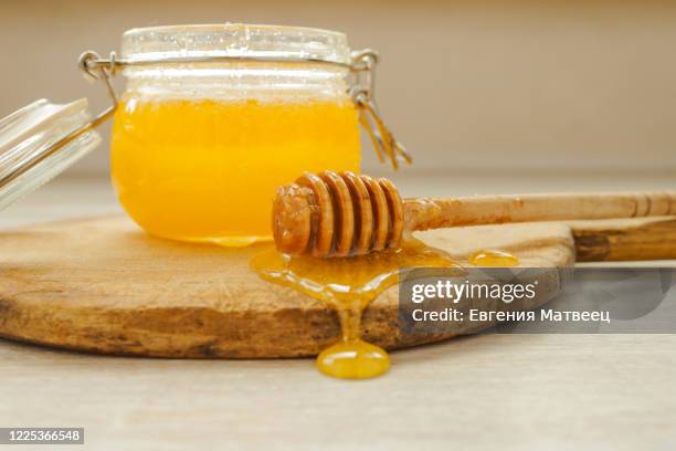 honey dripping from a wooden dipper and glass jar on old cutting board on white wooden rustic background - dippen stock-fotos und bilder