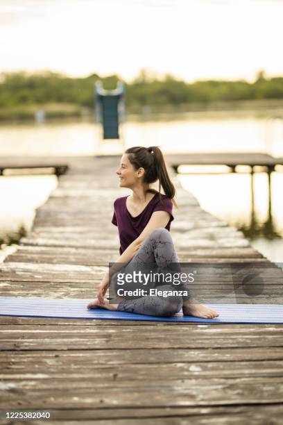 woman practicing yoga on lake pier - the twist stock pictures, royalty-free photos & images