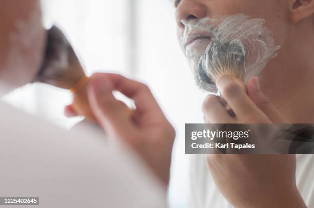 a young southeast asian man is using an old fashioned shaving equipment - pennello da barba foto e immagini stock