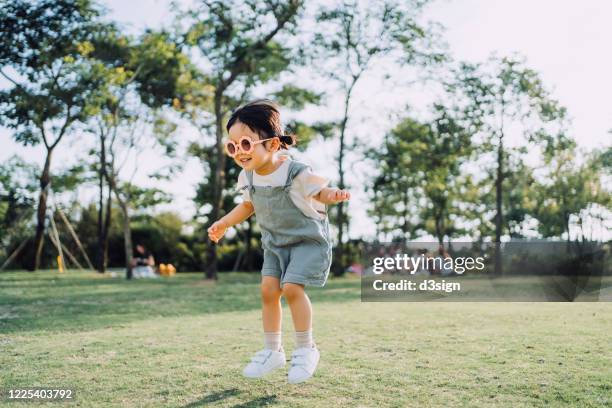 happy little asian toddler girl with flower-shaped sunglasses having fun outdoors enjoying summer days in the park - jumping girl stock pictures, royalty-free photos & images