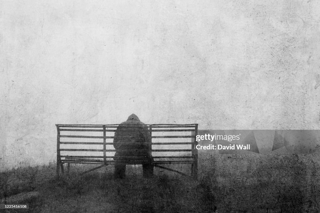 A mental health concept of mysterious figure back to camera, sitting on a bench alone. With a grunge, textured edit.