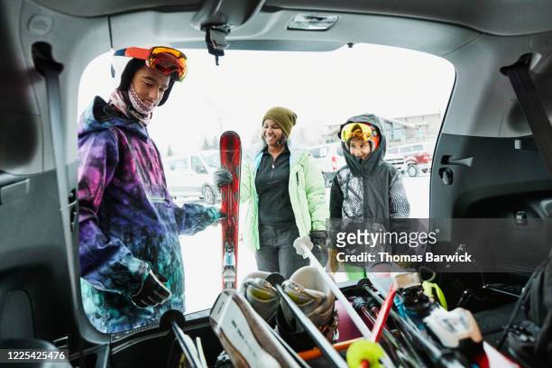teenage boy helping family get gear out of car before going skiing - friends skiing stock pictures, royalty-free photos & images