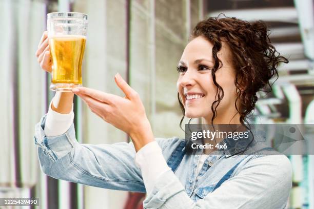 vrouwelijke handarbeider bij de distilleerderij die biboveralls draagt en alcohol houdt - brewmaster stockfoto's en -beelden