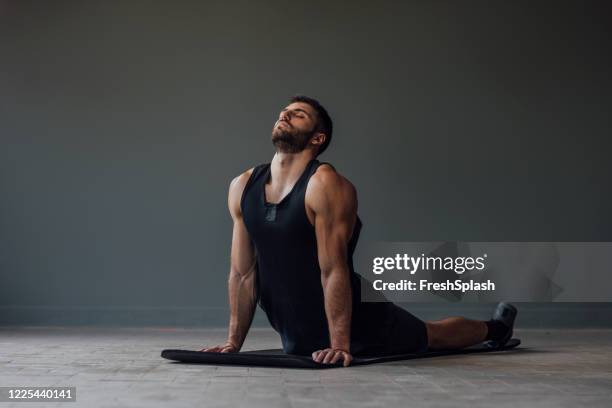 handsome muscular athlete doing yoga alone - stretching in the cobra pose - cobra stock pictures, royalty-free photos & images