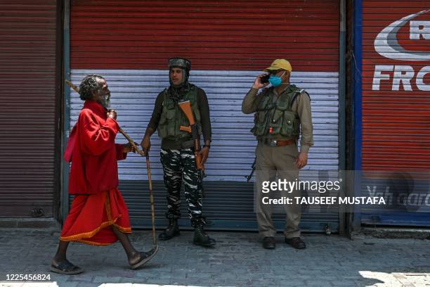 Sadhu walks past security personnel standing guard in Lal Chowk city square where most shops are shut on the fourth death anniversary of militant...