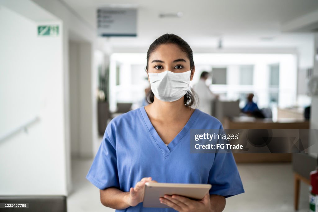Portrait of female nurse holding digital tablet at hospital using protective mask