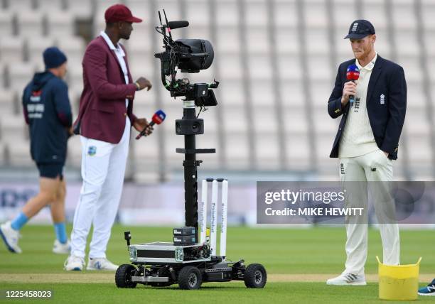 England's Ben Stokes and West Indies' Jason Holder hold microphones as they talk into a remote television broadcast camera, following the coin toss,...