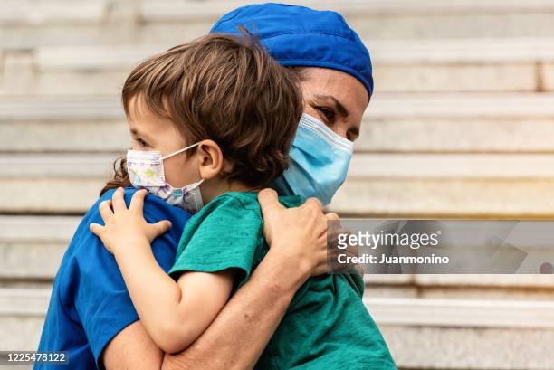 operatore sanitario maturo in posa abbracciando suo figlio dopo essere tornato dall'ospedale per combattere la pandemia di contagio - abbracciare una persona foto e immagini stock