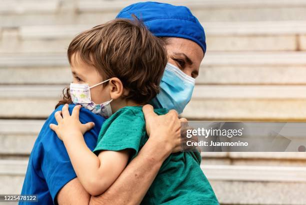 mature healthcare worker posing hugging her son after coming back from the hospital to fight contagion pandemic - leaving hospital stock pictures, royalty-free photos & images