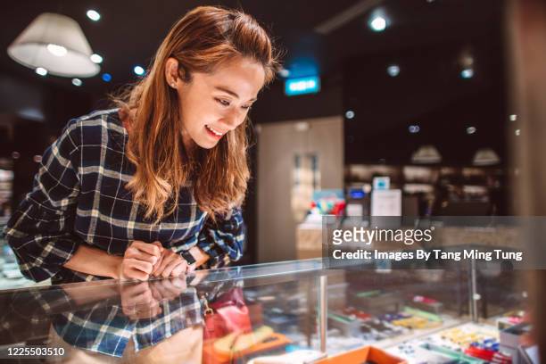 young woman choosing gifts at display cabinet  in a department store joyfully - vitrinekast stockfoto's en -beelden