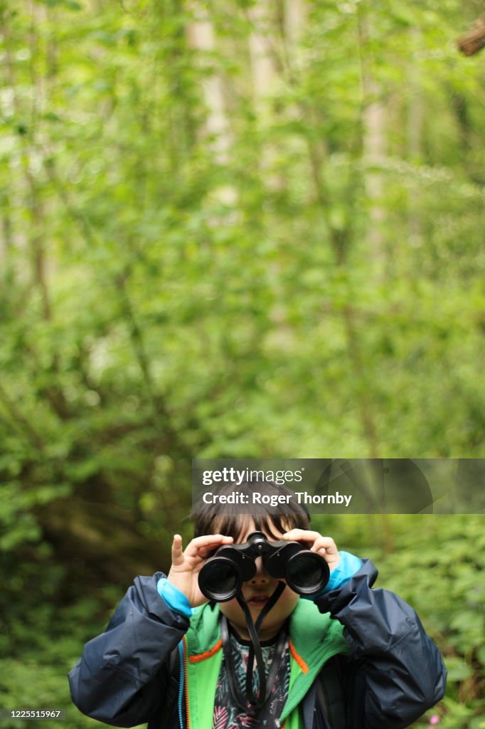 A young child looking at the camera with binoculars