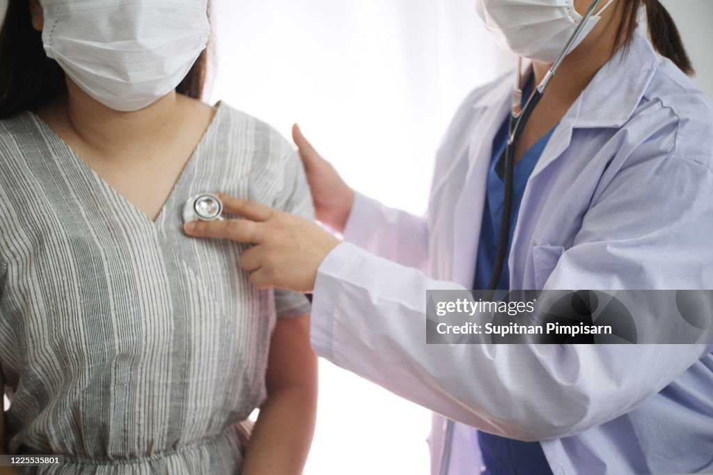 Kvinnlig medicin läkare som arbetar på bordet med konsultpatient, bär ansiktsmask för att skydda sig från virus Covid-19, Corona virus