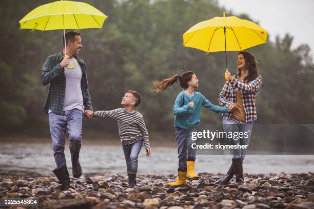 famille heureuse ayant l’amusement tout courant sur un jour pluvieux à la rive. - se protéger de la pluie photos et images de collection