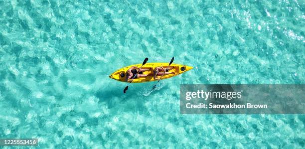 sporty caucasian couple kayaking on the crystal clear ocean. aerial view of two people in a kayak trudging the waters. - kayak stock-fotos und bilder