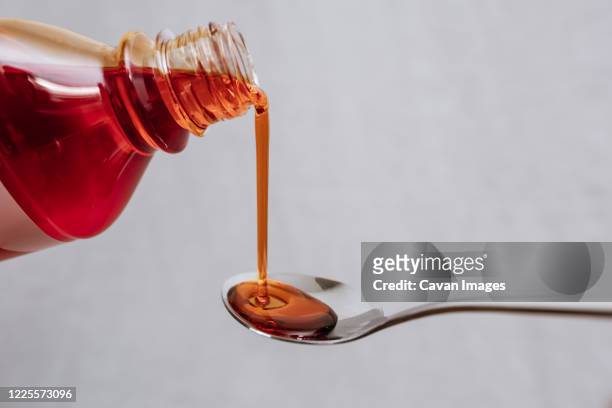 covid -liquid medicine bottle being poured out onto a metal spoon - hustenmittel stock-fotos und bilder