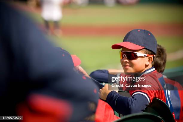 boy wearing sunglasses and smirking in baseball uniform - baseball fans stock pictures, royalty-free photos & images