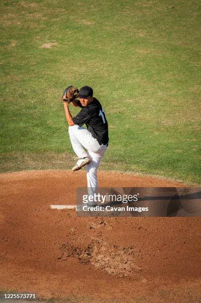 teen baseball player in black and white uniform in full wind up on the mound - kid baseball pitcher stock pictures, royalty-free photos & images