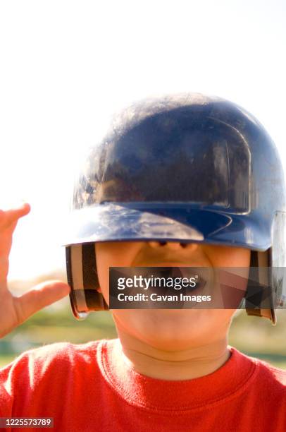 portrait of young boy missing a tooth with baseball helmet pulled down over his eyes - baseball helmet stockfoto's en -beelden