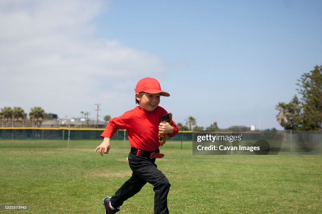 Young boy holding his glove and running across the Tball field