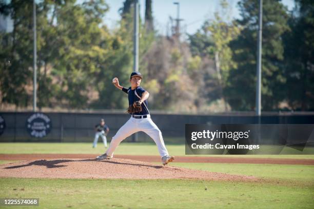 teen baseball player pitcher in blue uniform in full wind up on the mound - baseball pitcher stock-fotos und bilder