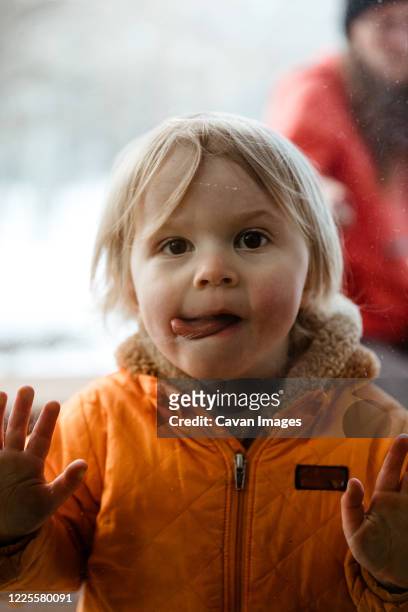 girl toddler pushes on window looks through glass with twisted tongue - miss you funny stock pictures, royalty-free photos & images