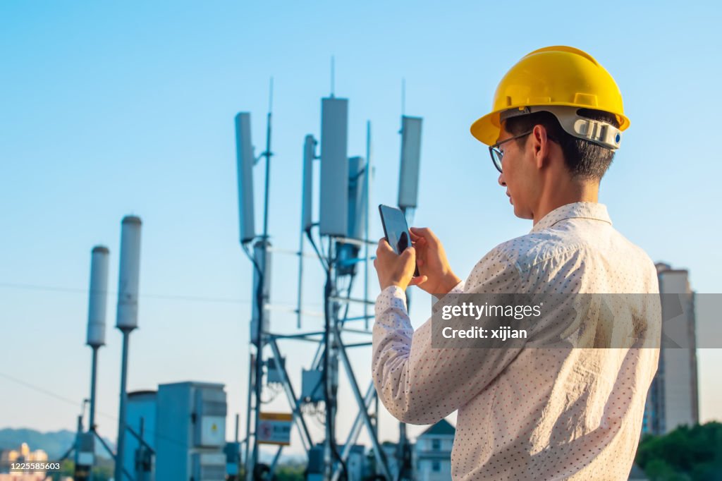 Engineer holding mobile phone testing the communications tower