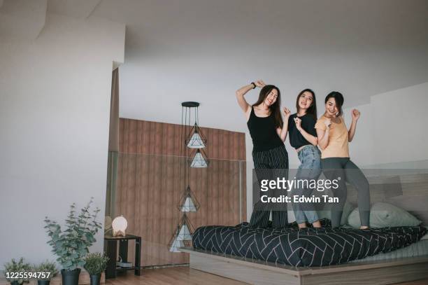 asiatische chinesische frau freunde tanzen auf dem bett im schlafzimmer spaßige zeit hören musik zweisamkeit bindung freude moment - girlfriends party stock-fotos und bilder
