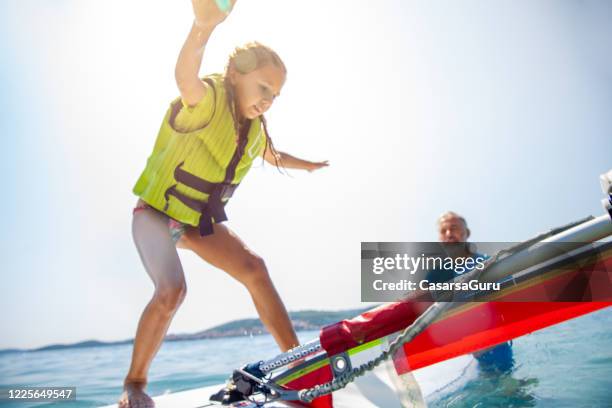 kleines mädchen versucht, die balance auf einem windsurf board zu bekommen - stock photo - windsurfbrett stock-fotos und bilder