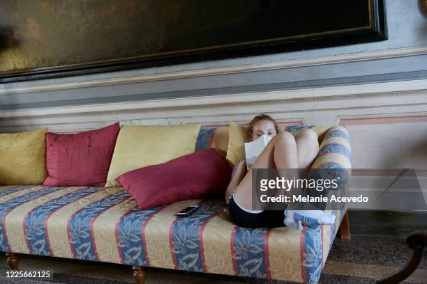 teenage girl with long red hair brown eyes and freckles lying back on couch looking at the camera resting her book on her face legs are bent and on the couch feet up next to decorative pillows - lying on back girl on the sofa stock-fotos und bilder