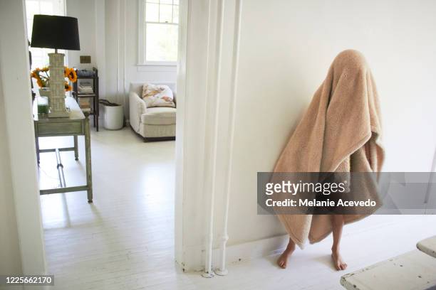 Young boy with brown curly hair brown eyes covering his body with brown blanket hiding his face you can only see his feet and legs standing in dinning room