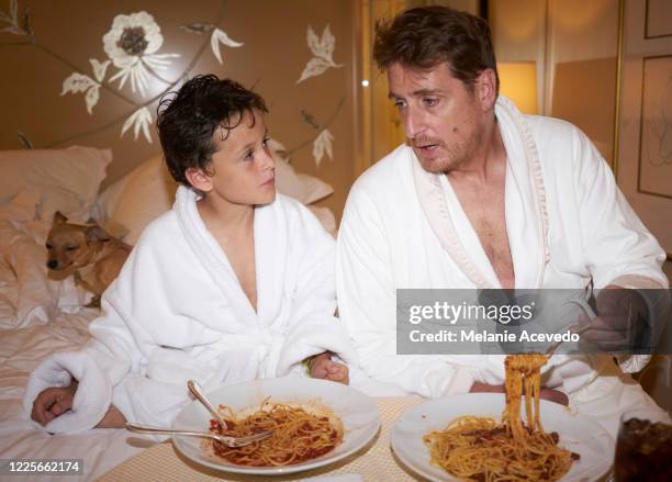young boy with brown curly hair brown hair brown eyes sitting up on bed with white bed sheets son and father wearing matching terry cloth robes - terry cloth stock pictures, royalty-free photos & images