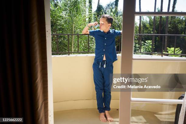 young boy with brown curly hair brown eyes drinking water standing on balcony wearing matching pajamas leaning over balcony railing summer morning drinking water holding glass cup to mouth standing up - leaning on elbows stock pictures, royalty-free photos & images