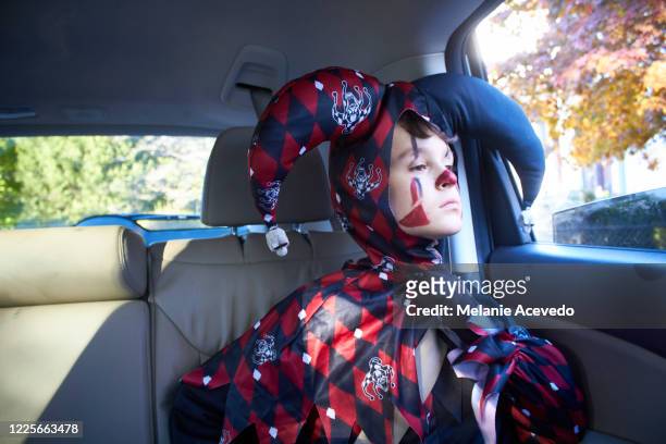 young boy with short brown curly hair and brown eyes close up holding small stuffed panda toy boy is sitting in the backseat of car looking outside of car window wearing a halloween costume