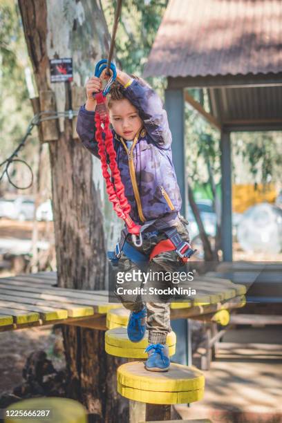 a young boy concentrates while navigating an obstacle course with ropes and harnesses. - ninja obstacle course stock pictures, royalty-free photos & images