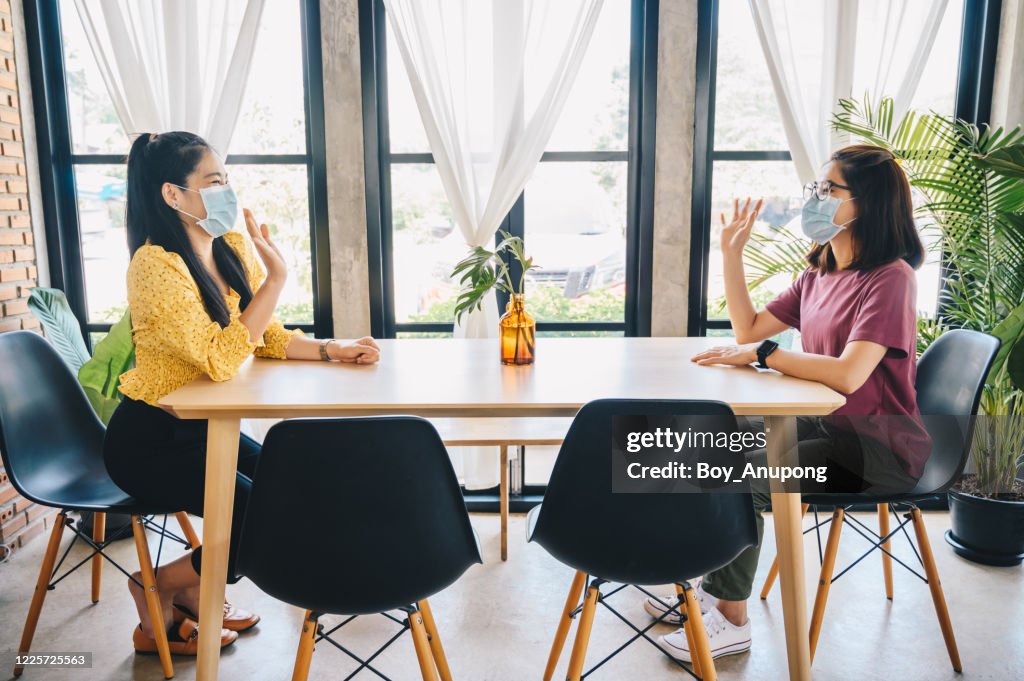 Two Asian woman meeting in cafe, wearing mask and keep social distancing for protection virus disease in Covid-19 pandemic.