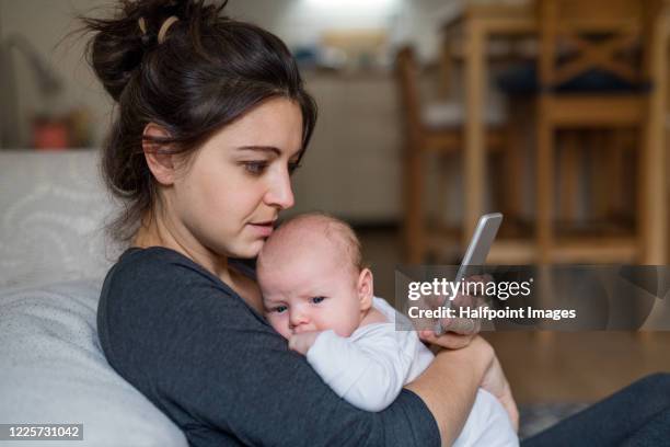 loving and affectionate mother holding newborn baby indoors at home, using smartphone. - new user stock-fotos und bilder