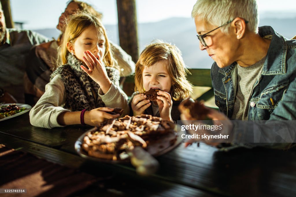 Small kids eating a pie with their grandmother on a terrace.