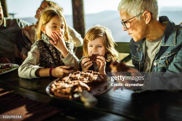 small kids eating a pie with their grandmother on a terrace. - sweetie pie stock pictures, royalty-free photos & images