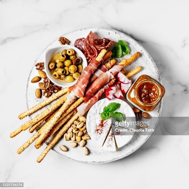 cheese plate assortment of french cheese served with nuts, salami, prosciutto, bread sticks, and preserves on a white cutting board on white background - ham salami stockfoto's en -beelden