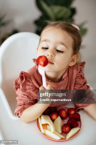 adorable cute caucasian blond toddler boy enjoy tasting different seasonal fresh ripe organic berries sitting in highchair at home living room - child eating juicy stock pictures, royalty-free photos & images