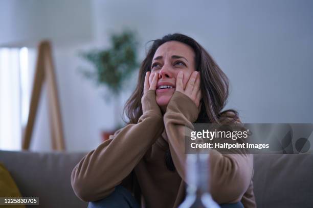 crying sad and depressed woman sitting indoors on sofa. - crying woman stock-fotos und bilder