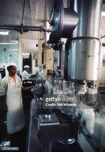 Worker stands at assembly line of machine filling milk bottles at dairy factory in Baghdad, circa 1978