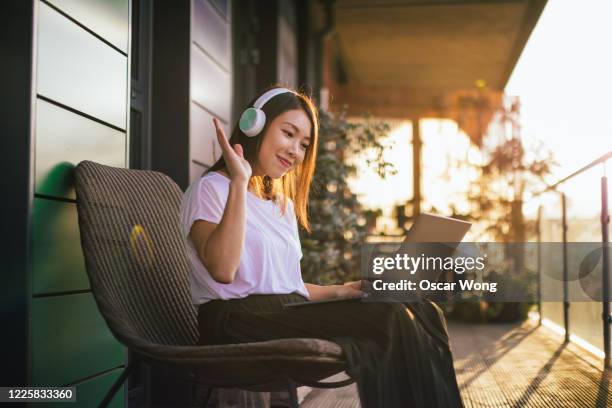 confident young woman with headphones having a conference call on laptop at the balcony - balcony stock photos et images de collection