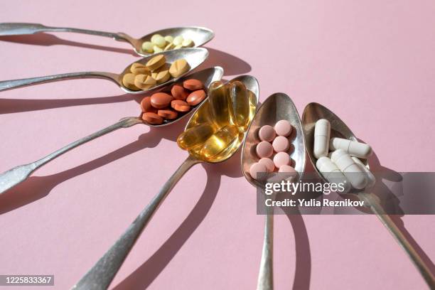 various of spoons with pills and tablets on the pink background - nahrungsergänzungsmittel stock-fotos und bilder