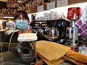 Barista woman with mask against covid-19, coronavirus, dispatching coffee and a sandwich wrapped in paper to take away with