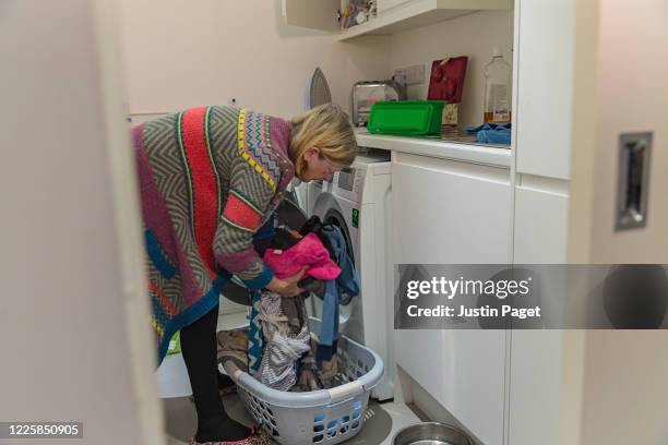 senior woman loading the washing machine - quarantaine stockfoto's en -beelden