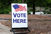 Vote here sign with an American flag to vote for elected government officials.